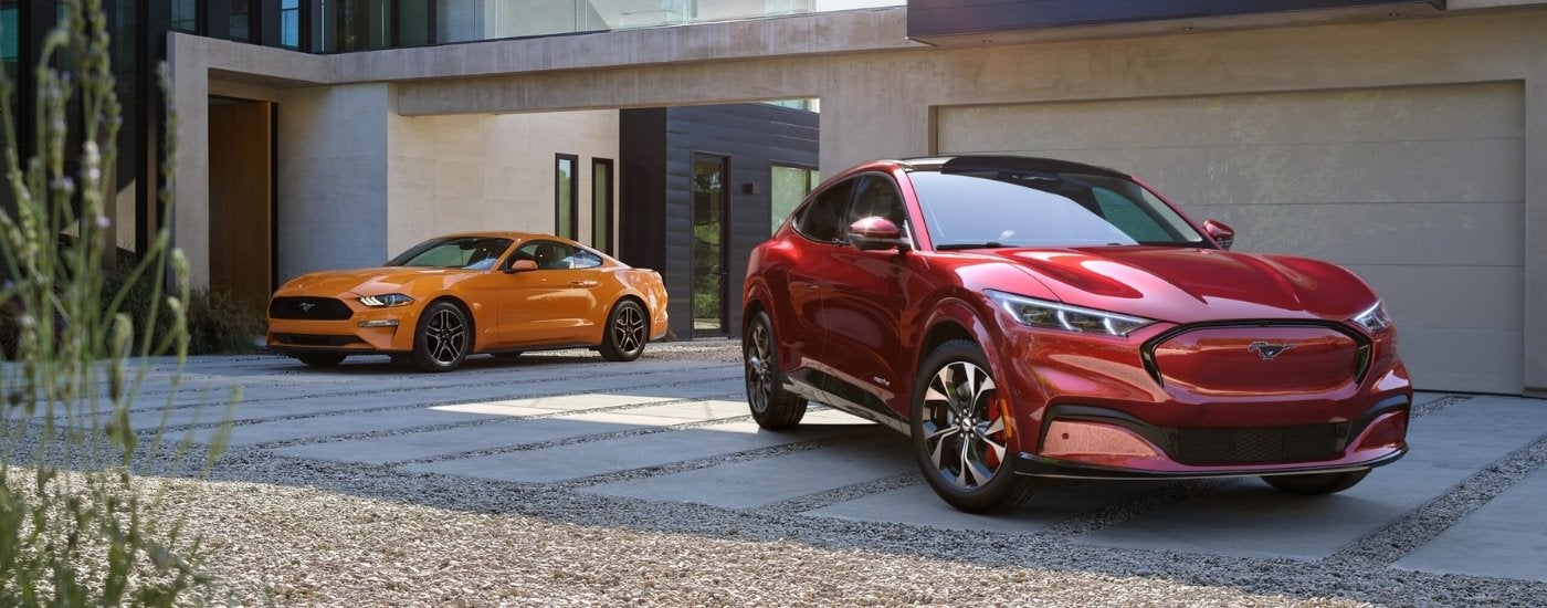 Orange 2021 Ford Mustang parked next to a red 2021 Ford Mustang Mach-E in a driveway
