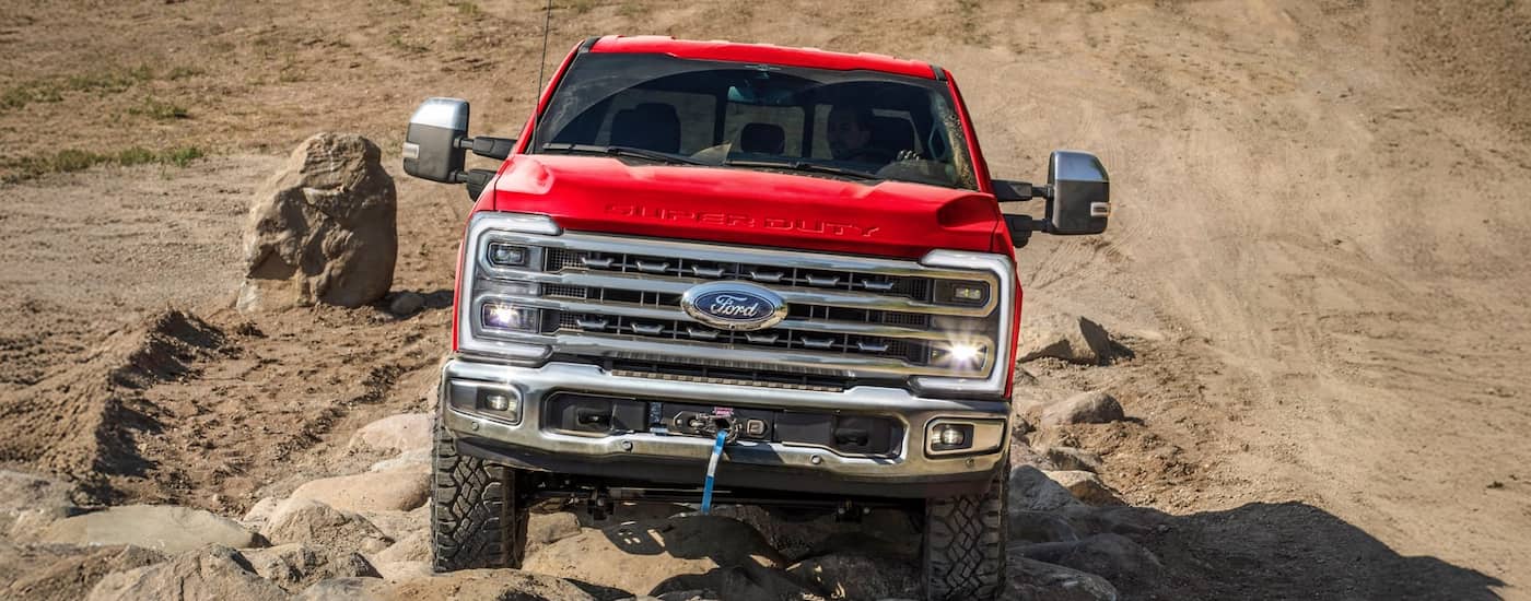Front of a red 2025 Ford F-250 driving off-road up a hill.