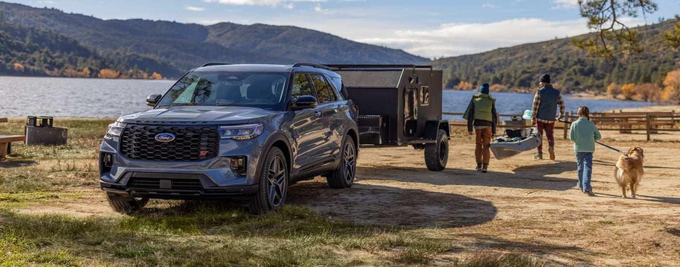 Blue 2026 Ford Explorer towing a trailer with a family near a lake.