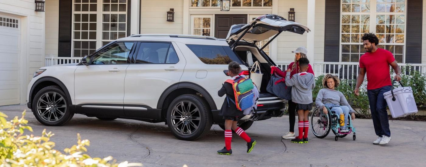White 2026 Ford Explorer parked in a driveway with a family loading the cargo area.