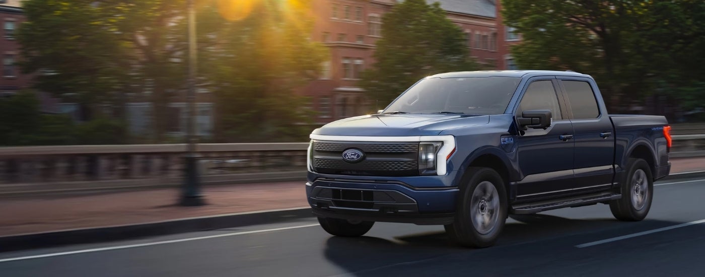 A blue 2025 Ford F-150 Lightning driving to a Ford dealer.