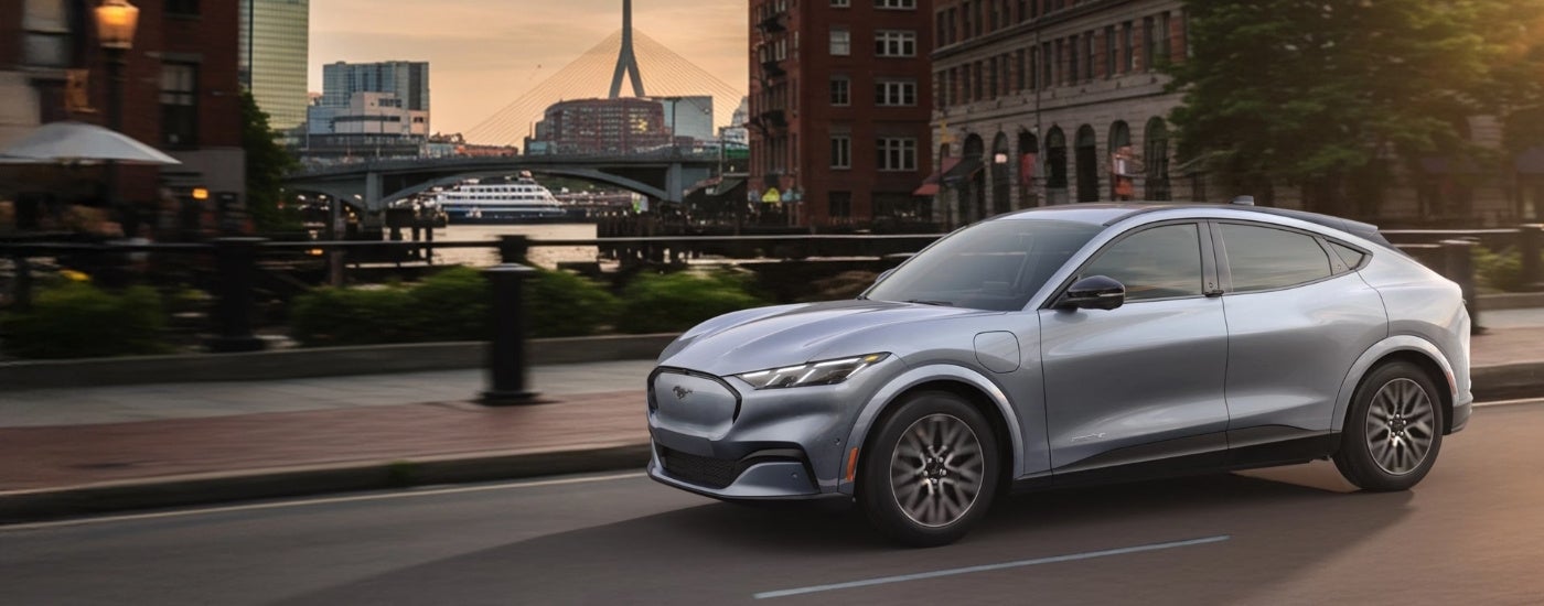 A silver 2025 Ford Mustang Mach-E driving on a city street.